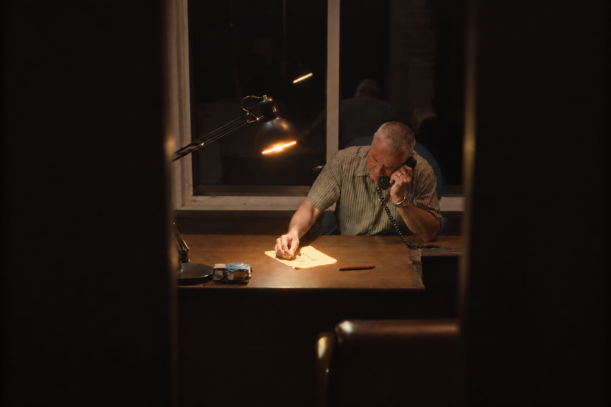 Illustrative scene, generated: an agent on the phone at his desk under a lamp, a market report page at his fingertips