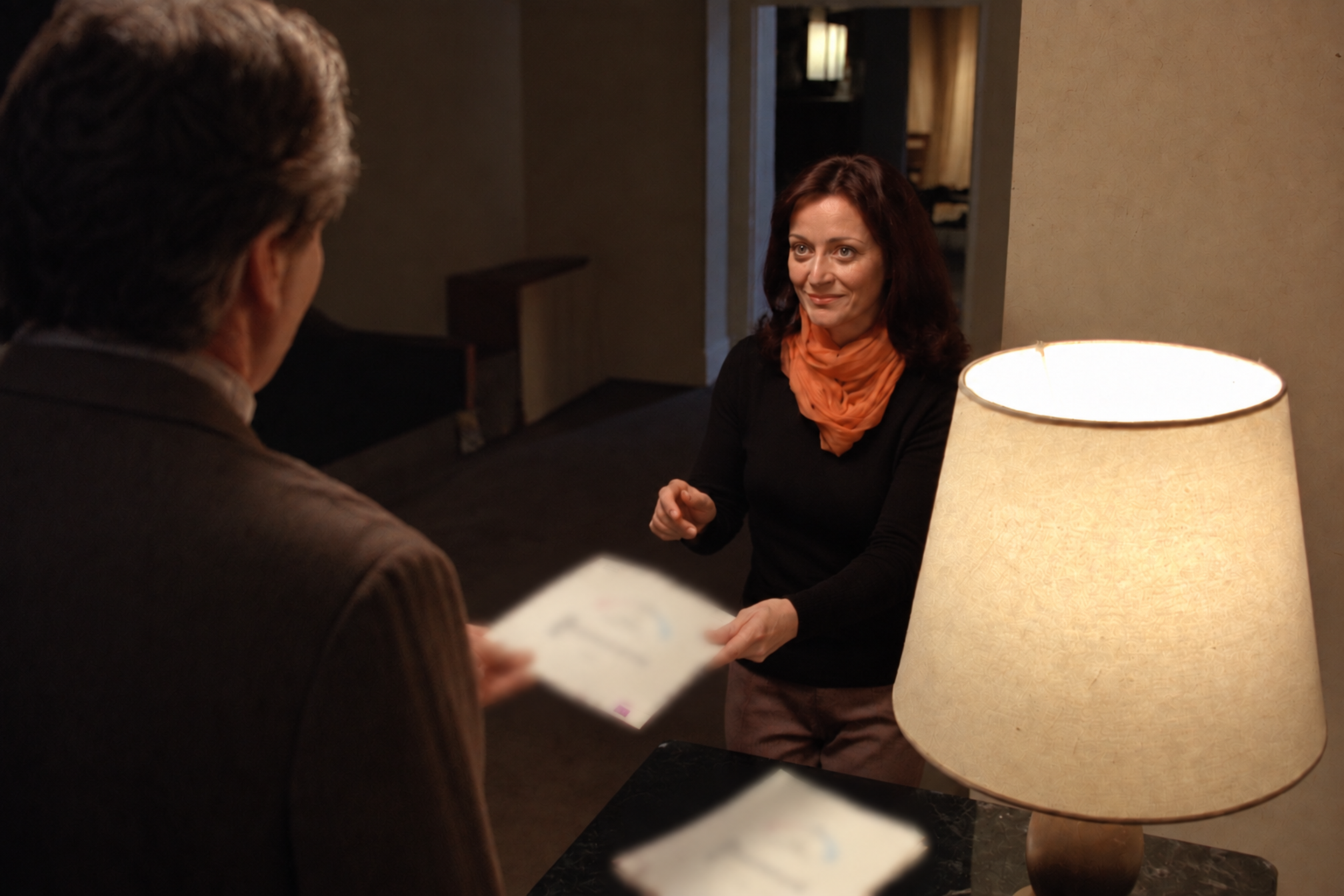 Illustrative scene, generated: an agent handing a visitor a market report page beside a table lamp
